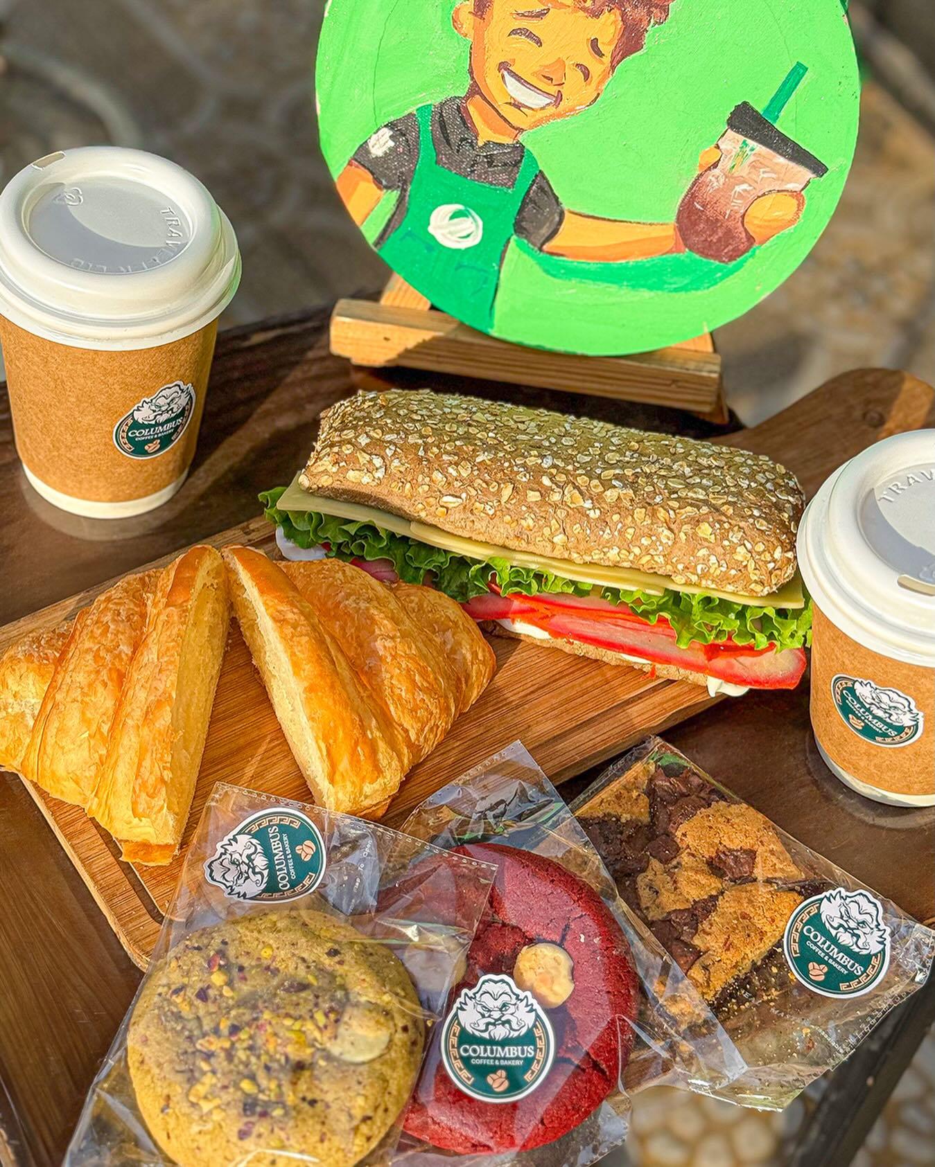 Columbus coffee cups beside fresh croissants, sandwiches and cookies